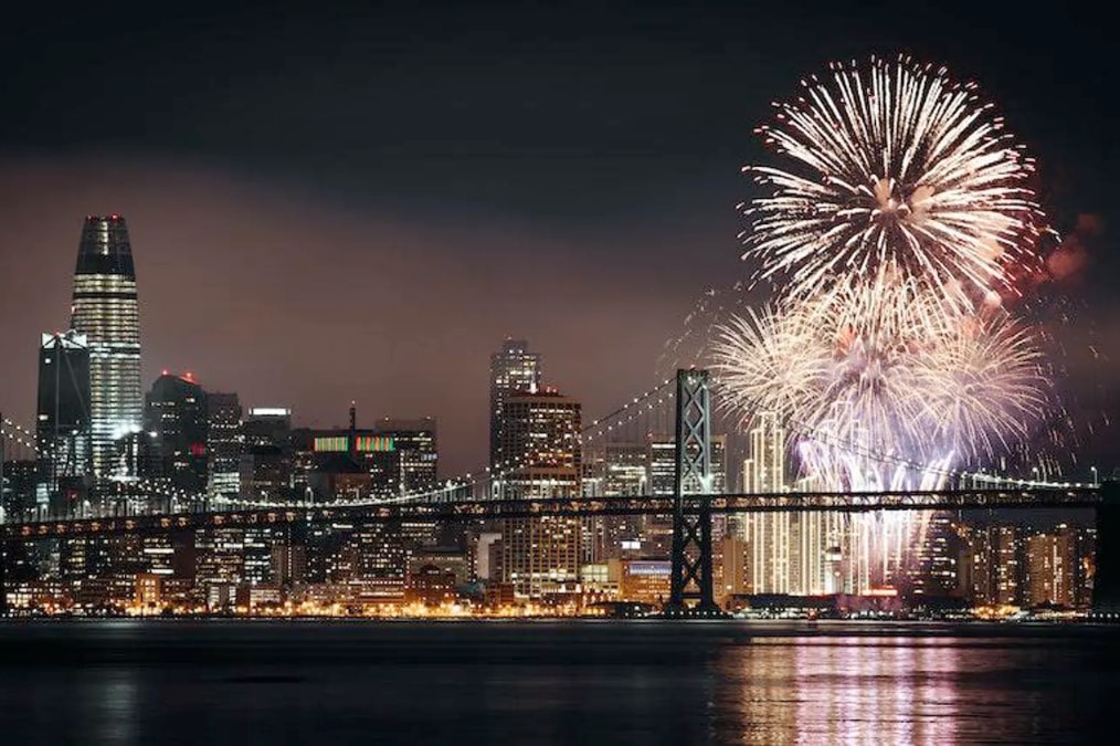 Photo of fireworks above the west span of the Oakland San Francisco Bay Bridge with the San Francisco skyline in the background